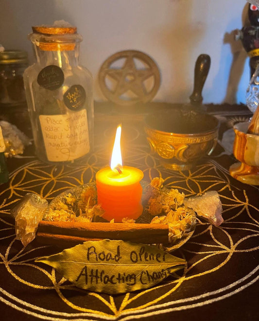 May include: A lit orange candle sits on a black circular surface with a gold geometric pattern. The candle is surrounded by dried flowers, a cinnamon stick, and a bay leaf with the words 'Road Opener Attracting Change' written on it. There is a clear glass jar with a cork lid and a label that reads 'Place herbs add water keep it safe from negative energy'.